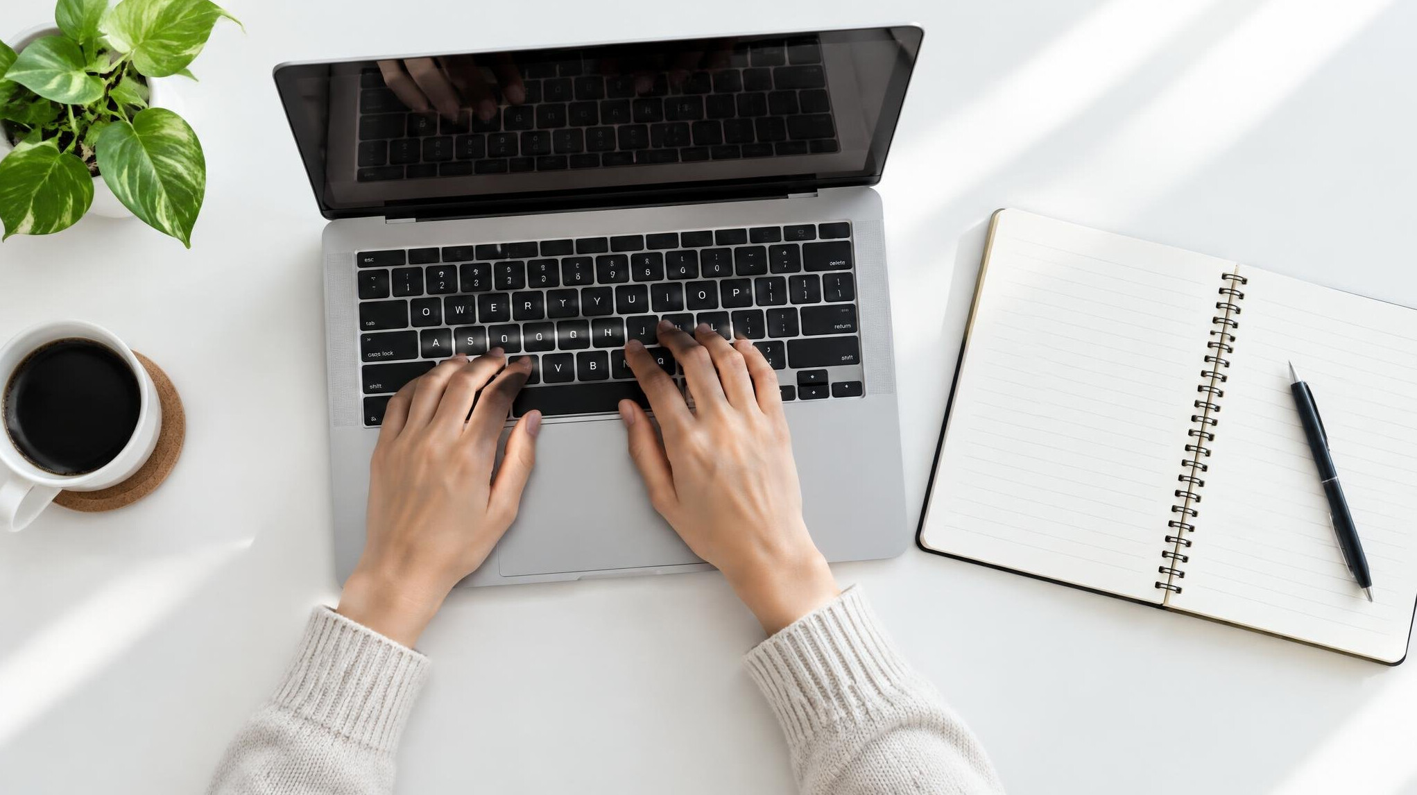 Hands typing on a laptop keyboard with a notebook nearby